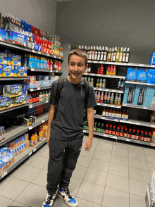 a young boy stands in a grocery store aisle filled with bottles of soda and other items