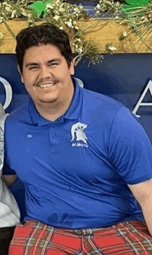 a man in a blue polo shirt and red plaid pants is smiling for the camera .