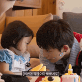 a boy and a little girl are looking at each other with a cake in the background