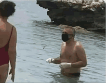 a man wearing a face mask and gloves is standing in the water .