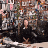 a woman in a black dress is sitting in front of a piano in a room filled with lots of stuff .