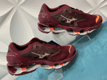 a pair of maroon and orange mizuno running shoes on display