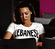 a woman wearing a white lebanese t-shirt sits in a chair