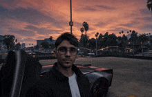 a man wearing glasses is standing in front of a car at sunset