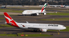 a qantas plane is parked next to an emirates plane on a runway