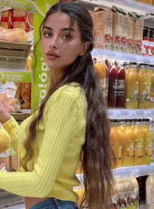 a woman in a yellow sweater stands in front of a sign that says organic on it