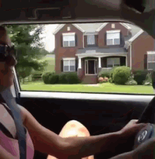 a woman in a pink tank top is driving a car in front of a brick house