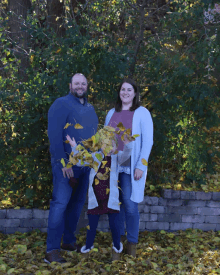 a man and a woman standing next to a little girl throwing leaves in the air