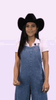 a woman wearing a cowboy hat and overalls is giving a thumbs up