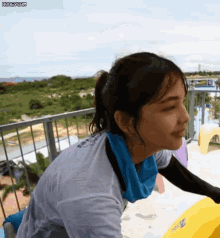 a woman wearing a white shirt and a blue towel around her neck is sitting on a yellow raft at a water park .