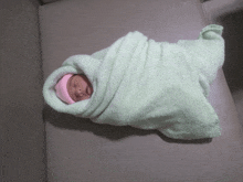 a newborn baby wrapped in a green blanket and a pink hat