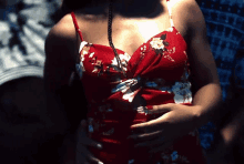 a woman in a red floral dress holds her hands on her stomach