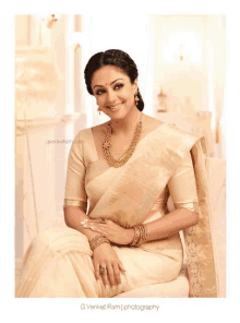 a woman wearing a white saree and gold jewelry is sitting on a couch