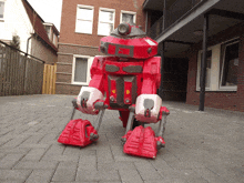 a red robot is standing on a brick sidewalk in front of a building