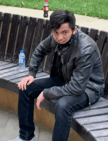 a man is sitting on a wooden bench with a bottle of water and a coca cola bottle in the background