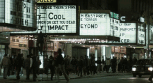 a crowd of people walking in front of a theater with a sign that says " cool " on it