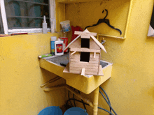 a small birdhouse sits on a yellow sink next to a bottle of clorox