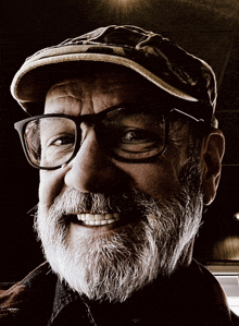 a man with a beard wearing glasses and a hat smiles