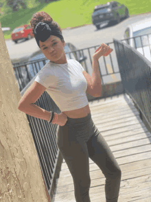 a woman in a white crop top and green pants stands on stairs