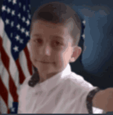 a young boy in a white shirt is standing in front of an american flag