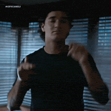 a man in a black shirt is dancing in front of a window with blinds