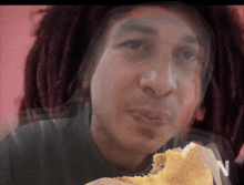 a man with dreadlocks is eating a sandwich with the letter n visible in the background