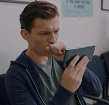 a man is holding a cell phone to his mouth while looking at it .