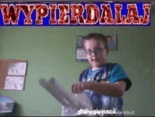 a boy holding a piece of paper in front of a sign that reads wypierdalaj