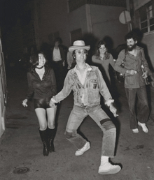 a black and white photo of a man in a cowboy hat holding hands with a woman