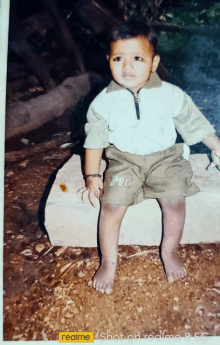 a young boy is sitting on a rock with a realme logo on the bottom