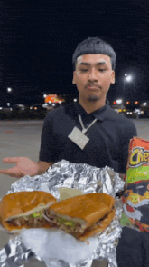a man is holding a sandwich and a bag of cheetos in front of him .