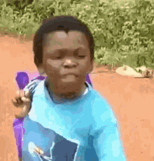 a young boy in a blue shirt is sitting in a chair on a dirt road and making a funny face .