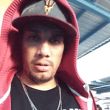 a man wearing a hat and a red hoodie looks at the camera