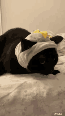 a black cat laying on a bed wearing a hat with a yellow bow