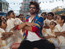 a man in a colorful jacket and sunglasses is surrounded by children