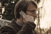 a man in glasses is talking on a cell phone .