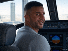 a man in a grey shirt is sitting in a cockpit of an airplane