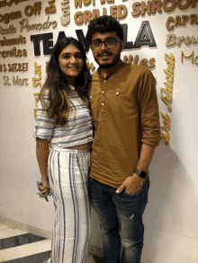 a man and a woman pose for a picture in front of a wall that says ' grilled shrimp '