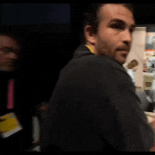 a man in a black shirt with a yellow lanyard around his neck is standing in a dark room