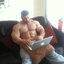 a shirtless muscular man is sitting on a couch using a laptop computer .