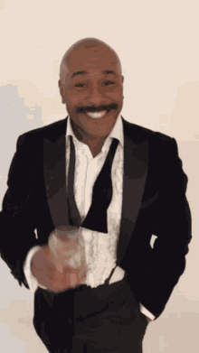 a man in a tuxedo with a mustache is holding a glass