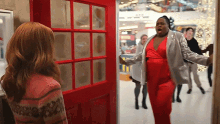 a woman in a red dress is standing next to a man in a silver jacket in front of a red door .