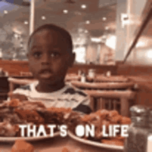 a young boy is sitting at a table with plates of food and a sign that says `` that 's on life '' .