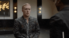 a man in a suit talks to another man in a black suit