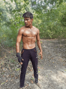 a shirtless man in black adidas pants stands in a forest