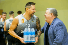 a basketball player with the number 12 on his jersey is holding a stack of oshee bottles