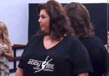 a woman in a black t-shirt is standing in front of a mirror in a dance studio .