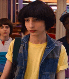 a young boy wearing a yellow t-shirt and a denim vest .