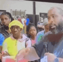 a man with a beard is speaking into a microphone in front of a crowd .