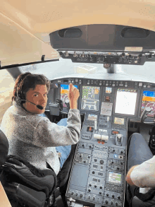 a man wearing a headset is giving a thumbs up in the cockpit of a plane